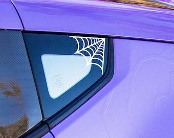May include: A purple car with a black spoiler and a white spiderweb decal on the rear window. The car has a black door handle and white wheels.
