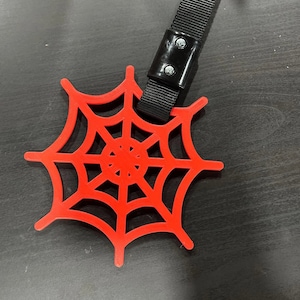 May include: Red plastic spider web with a black strap attached. The strap has a black buckle with two silver screws.