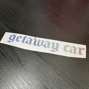 May include: A white vinyl sticker with iridescent glitter lettering that reads "getaway car" in a gothic font.
