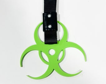 May include: A neon green biohazard symbol with a black strap and a black rectangular connector. The symbol is a three-lobed design, and the strap is made of a woven material.