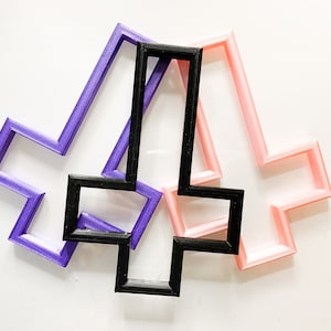 May include: Three upside-down crosses, one purple, one black, and one pink, are stacked on top of each other.