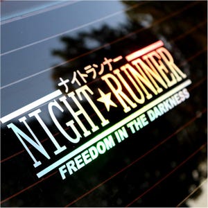May include: A sticker with the words "NIGHT RUNNER" in large white capital letters, with a star graphic. The text "FREEDOM IN THE DARKNESS" is below. Japanese characters are above the main text. The sticker has a gradient color effect.