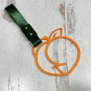 Può includere: Un cinturino in tessuto verde con due rivetti metallici argentati attaccati a un ritaglio a forma di pesca arancione.