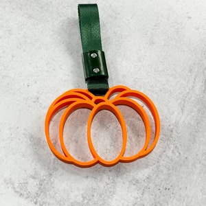May include: Orange pumpkin-shaped keychain with a green strap. The strap has two silver rivets.