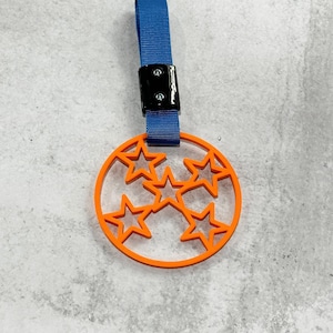 May include: Orange keychain with a five-pointed star design, attached to a blue strap with a black clip.