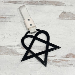 May include: Black and white heart-shaped keychain with a star design. The keychain is attached to a white strap with a white plastic buckle.