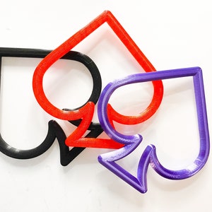 May include: Three plastic spades in different colors: black, red, and purple. The spades are layered on top of each other.