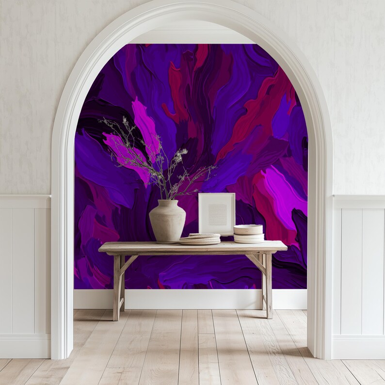 May include: A wooden table with a vase of dried flowers sits in front of an arched doorway. The wall behind the table is covered in a purple and pink abstract painting.