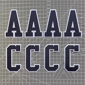 May include: Four black felt letters, two "A"s and two "C"s, with white outlines. The letters are arranged in two rows, with the "A"s on top and the "C"s on the bottom.