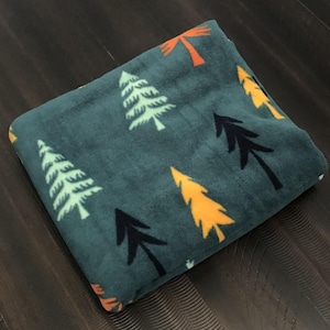 May include: A teal blue fleece blanket with a repeating pattern of stylized trees in various colors, including green, yellow, orange, and black.