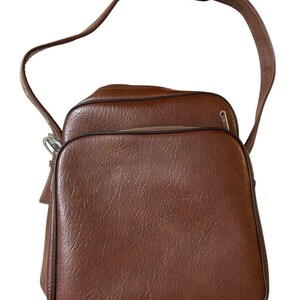 Puede incluir: Bolso de hombro de cuero marrón con superficie texturizada. El bolso tiene un asa superior y una correa larga ajustable. Cuenta con un compartimento principal con cremallera y un bolsillo frontal más pequeño. Estilo vintage.