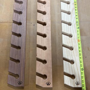 Puede incluir: Tres soportes de pared verticales de madera con siete recortes circulares cada uno, en tonos de madera oscuro, medio y claro. Una cinta m&eacute;trica amarilla colocada a lo largo del soporte derecho muestra una longitud de unos 71 cent&iacute;metros.