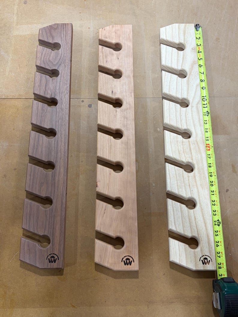 Puede incluir: Tres soportes de pared verticales de madera con siete recortes circulares cada uno, en tonos de madera oscuro, medio y claro. Una cinta m&eacute;trica amarilla colocada a lo largo del soporte derecho muestra una longitud de unos 71 cent&iacute;metros.