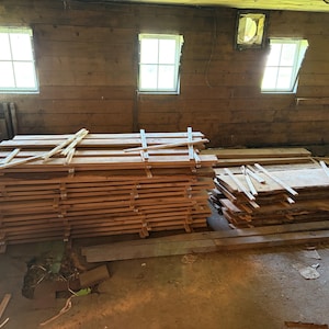 Puede incluir: Una gran pila de tablas de madera rectangulares de color marr&oacute;n claro dispuestas en capas horizontales. La madera est&aacute; cuidadosamente apilada con finos espaciadores de madera entre las tablas, creando un aspecto estructurado y uniforme.