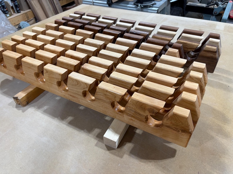 Puede incluir: Un soporte de madera con m&uacute;ltiples filas de ranuras talladas dise&ntilde;adas para sostener objetos. El soporte est&aacute; construido con madera de color claro en la parte delantera y cambia a tonos de madera marr&oacute;n oscuro y rico hacia la parte trasera.