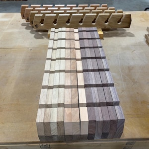 Puede incluir: Una colecci&oacute;n de estantes de madera con ranuras en &aacute;ngulo para almacenamiento. Los estantes est&aacute;n hechos de madera clara y madera de tono nogal m&aacute;s oscuro, dispuestos en filas paralelas con un patr&oacute;n de cuadr&iacute;cula de segmentos verticales y horizontales.