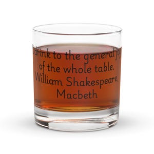 Peut inclure: Un verre transparent rempli d'un liquide brun. Le verre porte un texte noir qui dit : « Je bois à la joie générale de toute la table. William Shakespeare, Macbeth. »