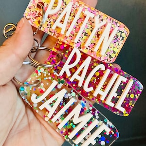 May include: Three colorful keychains with the names "PAITYN", "RACHEL", and "JAIMIE" embedded in clear resin with colorful glitter.