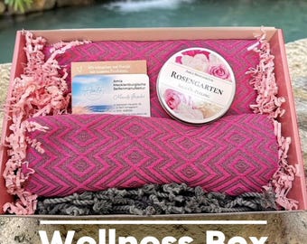Puede incluir: Una caja de regalo que contiene un tejido plegado con estampado magenta y gris, una lata redonda con la etiqueta Rosengarten y una tarjeta de visita de Amla Mecklenburgische Seifenmanufaktur. La caja incluye relleno de papel rosa sobre piedra.