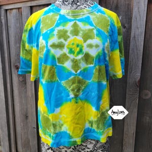May include: A tie-dye t-shirt with a blue, yellow and green colour scheme. The shirt has a circular pattern in the centre and a geometric pattern throughout.