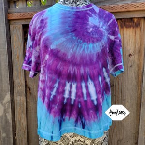 May include: A tie-dye t-shirt with a purple and blue swirl pattern. The shirt has a crew neck and short sleeves.