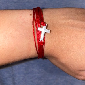May include: A red string bracelet with a silver cross charm.