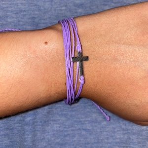 May include: A purple braided bracelet with a silver cross charm.
