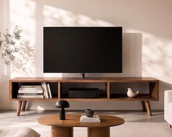 May include: A living room featuring a low-profile wooden media console with open shelving, a cream-colored tufted lounge chair, an oval wooden coffee table with cylindrical legs, and a cream-colored sofa, all arranged on a light-colored area rug.