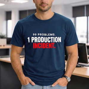 Pode incluir: T-shirt azul marinho com o texto "99 PROBLEMS. 1 PRODUCTION INCIDENT." em branco e vermelho. A t-shirt é de manga curta e tem gola redonda.