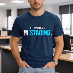 May include: Navy blue crew neck t-shirt with the text "IT WORKED IN STAGING." in white and light blue. The shirt is made of a soft material and is suitable for casual wear. The t-shirt is a classic fit.