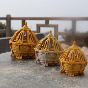 May include: Three gold-colored decorative cages of varying sizes. The cages are intricately designed with a geometric pattern and have a domed top.
