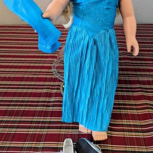 Puede incluir: Un vestido azul brillante con ribete plateado, una faja de tela azul y zapatos plateados. El vestido es plisado y tiene un escote de coraz&oacute;n.