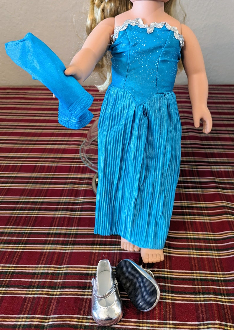Puede incluir: Un vestido azul brillante con ribete plateado, una faja de tela azul y zapatos plateados. El vestido es plisado y tiene un escote de coraz&oacute;n.