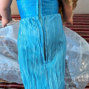 Puede incluir: Un vestido azul y plateado con una cremallera en la espalda. El vestido tiene un corpi&ntilde;o brillante y una falda plisada.