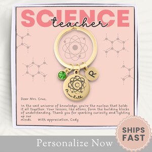 May include: A gold-colored keychain with a charm that says "Science Teacher" and a small atom charm. The keychain is in a pink box with the words "Ships Fast" on a sticker.