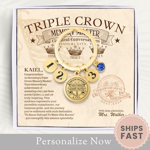 May include: A gold-colored triple crown memory master keychain with blue gemstones and a personalized inscription. The keychain is in a white box with a gold background and the text "Triple Crown Memory Master" and "To Know God and To Make Him Known".