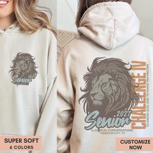 May include: A beige hooded sweatshirt featuring a brown lion graphic on the front left chest and a larger version on the back. The back design includes the text "Senior 2027", "Challenge IV", "To know God and to make Him known", and "Classical Conversations Missouri City, TX".