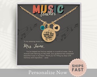 May include: A gold necklace with a charm that says "It's a good day to make music" and a small heart charm. The necklace is in a gift box with a message that says "To my amazing music teacher, Mrs. Jaime, You've helped me find my melody in a world of notes. Like a musical note dancing on the staff, your guidance has composed beautiful tunes in my heart. Thank you for filling my days with harmony and inspiration. -Jane"
