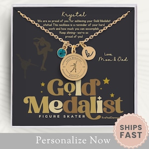 May include: Gold Medalist figure skater necklace with a gold charm featuring a figure skater and the words "Gold Medalist Krystal". The necklace is displayed in a white box with a black background and the words "Love, Mom & Dad".