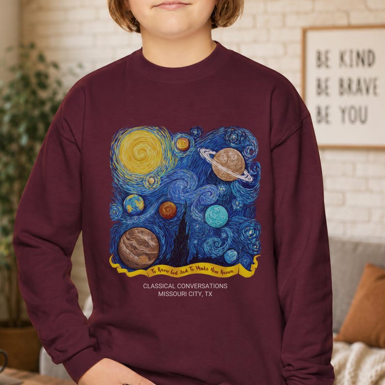 May include: A maroon long-sleeve sweatshirt featuring a graphic of swirling blue cosmic patterns, various planets, and a yellow banner with the text "To Know God And To Make Him Known" above "CLASSICAL CONVERSATIONS MISSOURI CITY, TX".