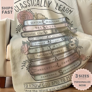 May include: A cream-colored throw blanket draped over a sofa, featuring a stack of illustrated books with titles like "Sentence Diagrams" and "Faces of History." The blanket has floral accents and the text "Classically Learn."