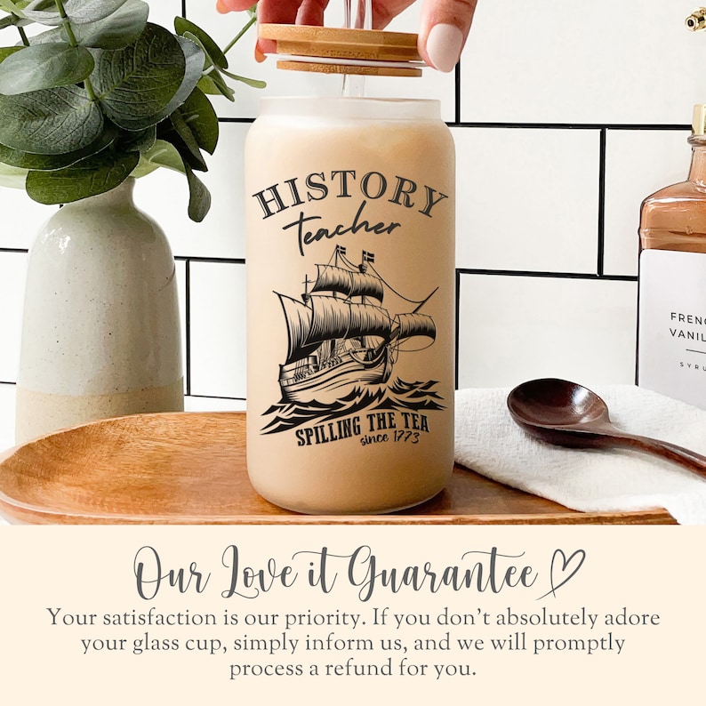 May include: A frosted glass cup with a wooden lid and a straw. The cup has a black and white illustration of a ship and the text "HISTORY teacher SPILLING THE TEA since 1773".