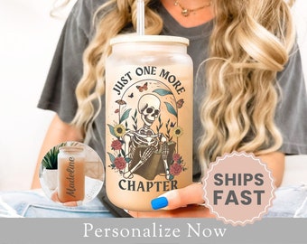 May include: A white tumbler with a black and white skeleton reading a book. The tumbler has the text "Just One More Chapter" and floral designs.
