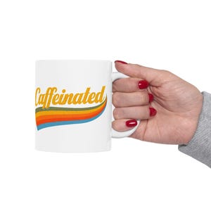 May include: White ceramic mug with a rainbow design and the text "caffeinated" in yellow.