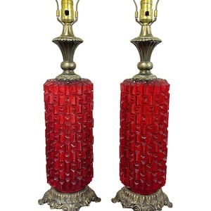 Peut inclure: Paire de lampes de table vintage avec des corps cylindriques en verre rouge texturé. Les lampes ont des bases et des raccords en métal de couleur laiton, et sont conçues avec une esthétique classique du milieu du siècle. Ce sont des luminaires décoratifs.