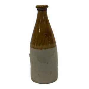 Pode incluir: Garrafa de grés vintage de duas cores. A parte superior é castanha quente, passando para um bege claro na base. A garrafa tem um gargalo estreito e um topo arredondado, sugerindo que pode ter sido usada para líquidos.