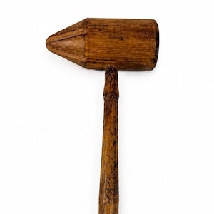 May include: A wooden mallet with a dark brown finish. The mallet has a rectangular head and a long, tapered handle. The wood grain is visible on both the head and the handle. The mallet is set against a white background.