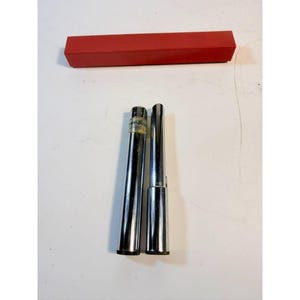 May include: Two chrome-colored metal tools with a red rectangular box. One tool is cylindrical with a label, the other is a tapered cylinder. The box is a solid, bright red color. The tools are on a white surface.