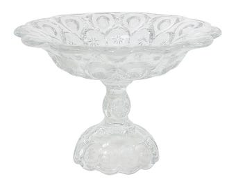 Op de afbeelding: Een heldere glazen schaal op voet met een geschulpte rand en een ingewikkeld patroon van sterren en halve manen. De schaal wordt ondersteund door een gedetailleerde steel en voet, perfect voor het presenteren van fruit of decoratieve items.
