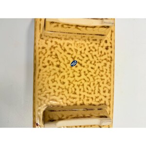 K&ouml;nnte beinhalten: Ein rechteckiger Aschenbecher aus Keramik mit einer strukturierten, gesprenkelten Oberfl&auml;che in Beige- und Braunt&ouml;nen. Er hat zwei eingebaute Ablagen und einen kleinen blauen Aufkleber mit der Aufschrift "Made in Japan".